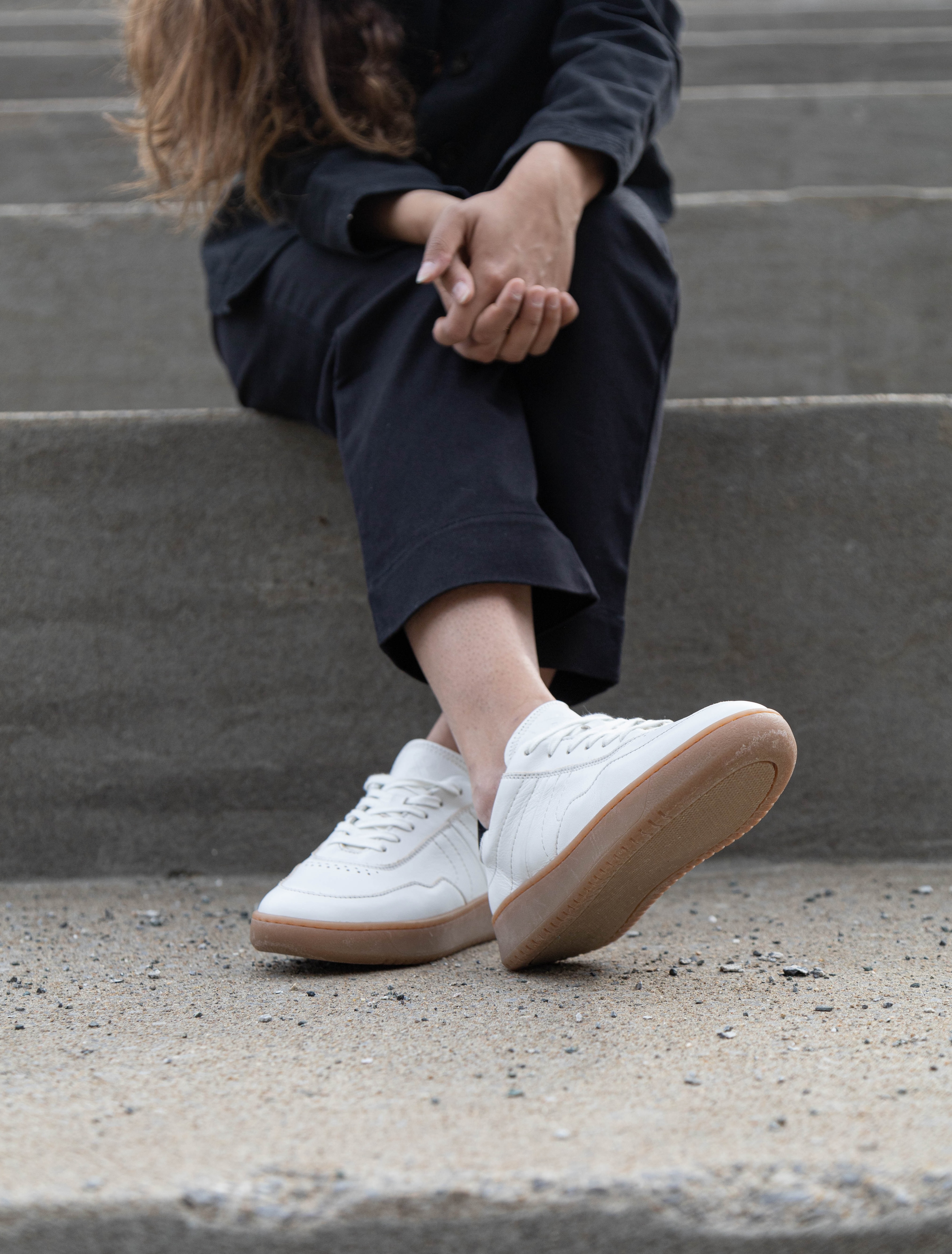 Lady with crossed legs at the ankles wearing simple & strange sneaker.
