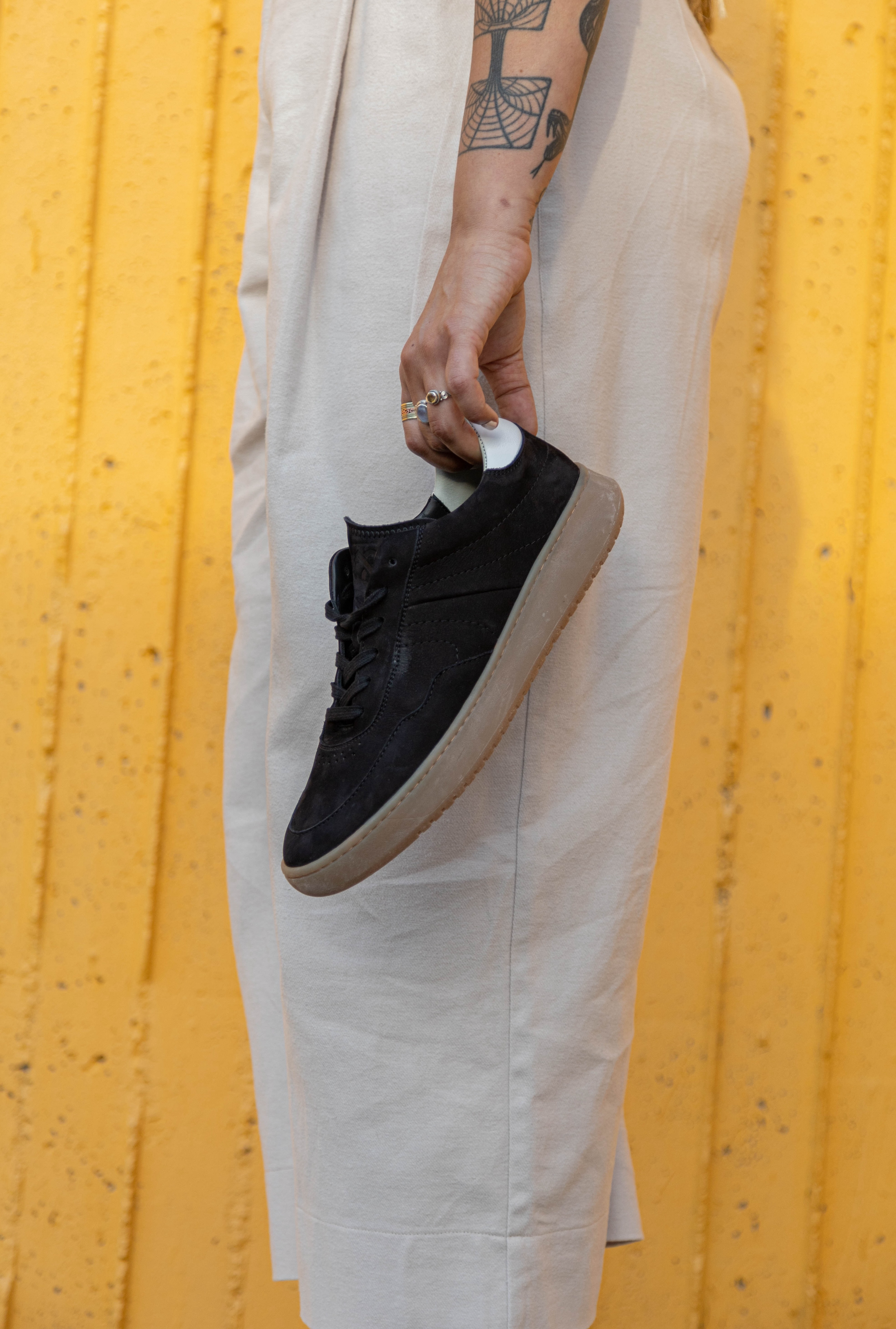 Lady with tattoos holding a pair of simple & strange sneaker.